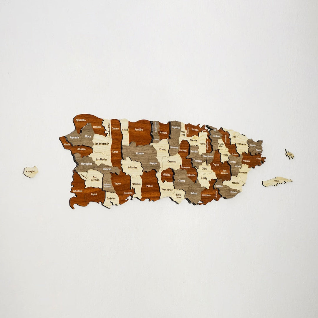 Layered wooden map of Puerto Rico on a white wall, each municipality cut as a separate piece in cream, walnut, gray and red-brown wood