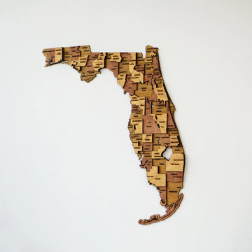 3D wooden Florida map with county names in layered wood tones, shown on a plain white wall
