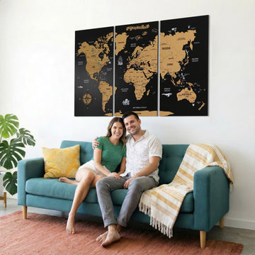 Black three-panel cork world map above a teal sofa with a smiling couple, closer view