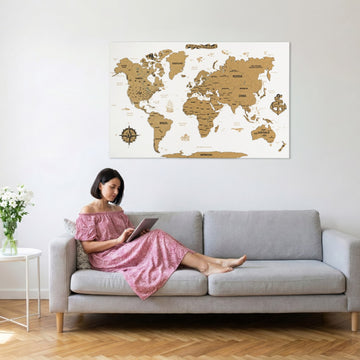 White cork push pin world map above a gray sofa where a woman in a pink dress reads a tablet