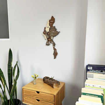 Myanmar wooden wall map above a chest of drawers beside a stack of books