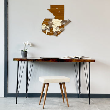 Multicolor wooden Guatemala map hung high above a hairpin-leg desk and white stool in a wide room view