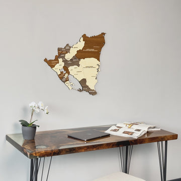 Wooden Nicaragua map on a gray wall above a desk with an orchid, angled from the right