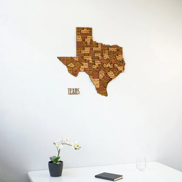 Wooden Texas wall map and lettering on a white wall above a desk edge with an orchid, front view