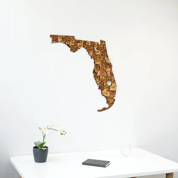 Layered wooden Florida wall map above a white desk, with a potted orchid beside it