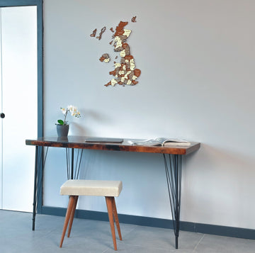Small United Kingdom wooden wall map above a desk with a cream stool in front of a white door