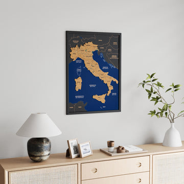 Black-framed Italy cork wall map above a low sideboard, lamp and small picture frames in the foreground