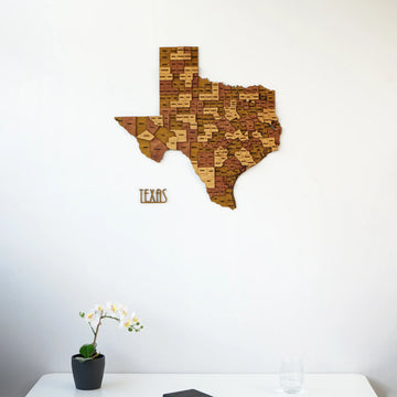 Texas wooden wall map and lettering on a white wall, framed higher with a desk and orchid at the bottom