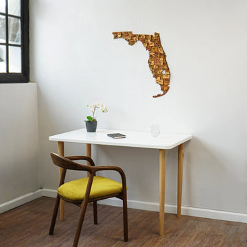 Wooden Florida wall map in a bright room corner above a white desk, window at left