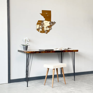Wooden Guatemala wall map centered above a desk and stool, wide room view with a gray tile floor