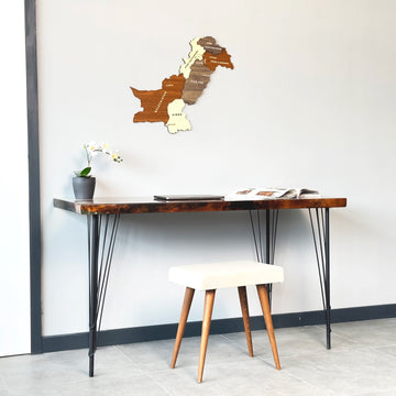 Pakistan wooden wall map on a white wall above a desk with a cream stool, medium view
