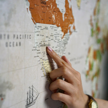 Close-up of a finger touching the United States on the sepia canvas world map with a sailing ship drawing