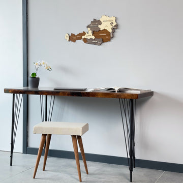 Austria wooden wall map beside a gray wall edge, above the left side of a desk with a cushioned stool