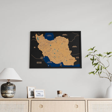 Black-framed Iran cork wall map, straight-on view above a sideboard with a lamp and framed prints
