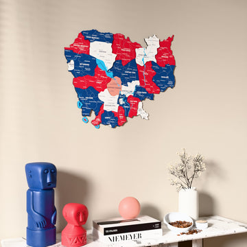 Flag colored Cambodia wooden wall map on a beige wall above a console with figurines