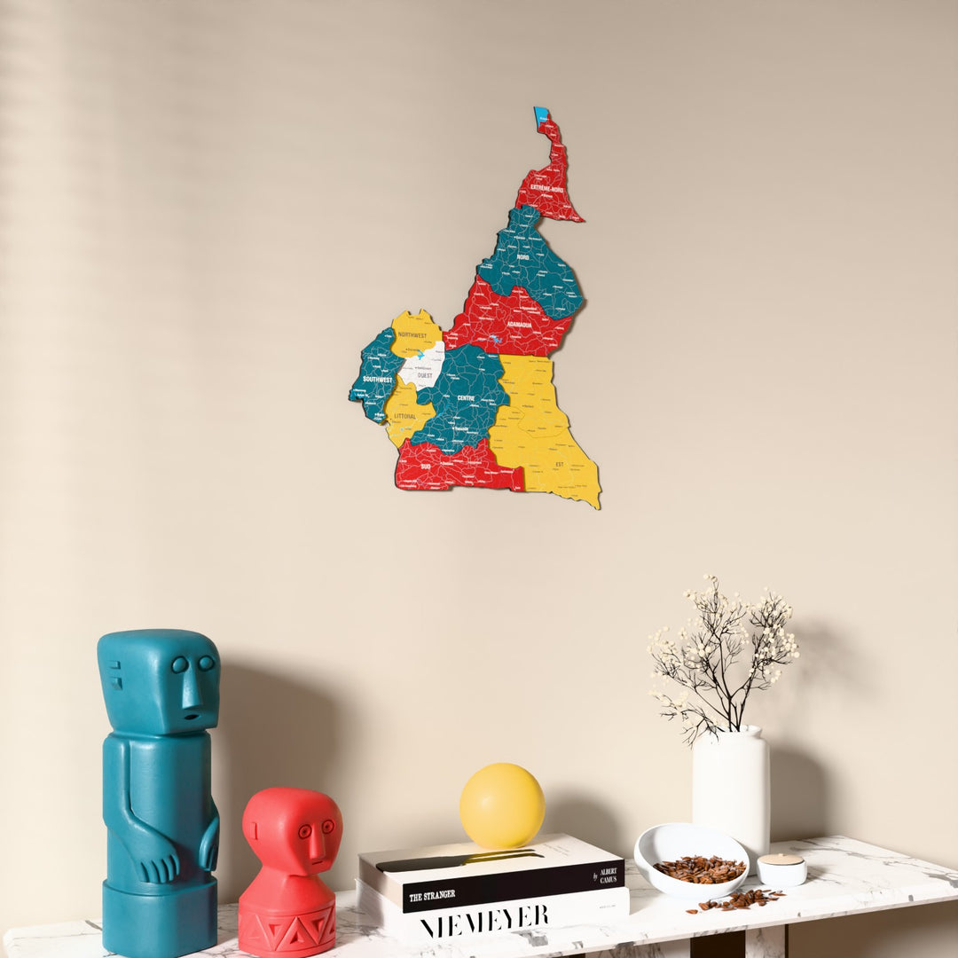 Flag colored Cameroon wooden wall map on a beige wall above a console with figurines