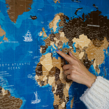 Navy blue canvas world map with sailing ship drawings, a hand pointing at Europe and Africa