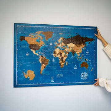 Navy blue ocean canvas world map hung on a white wall, hands holding the edges