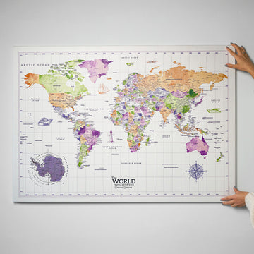 Watercolor world map canvas being hung on a white wall, full map with Antarctica and compass visible