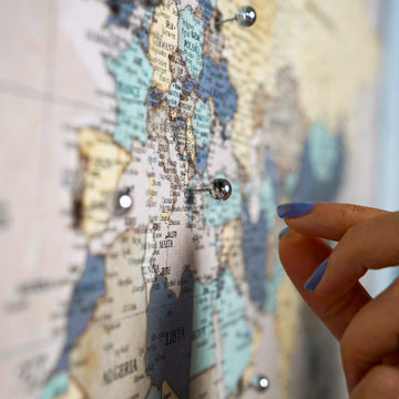 Blurred close-up of a finger placing a silver pin on Europe on the muted vintage world map canvas