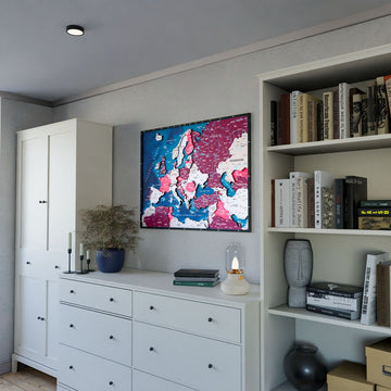 Wooden Europe map with rivers in Crimson, above a white dresser beside a bookshelf