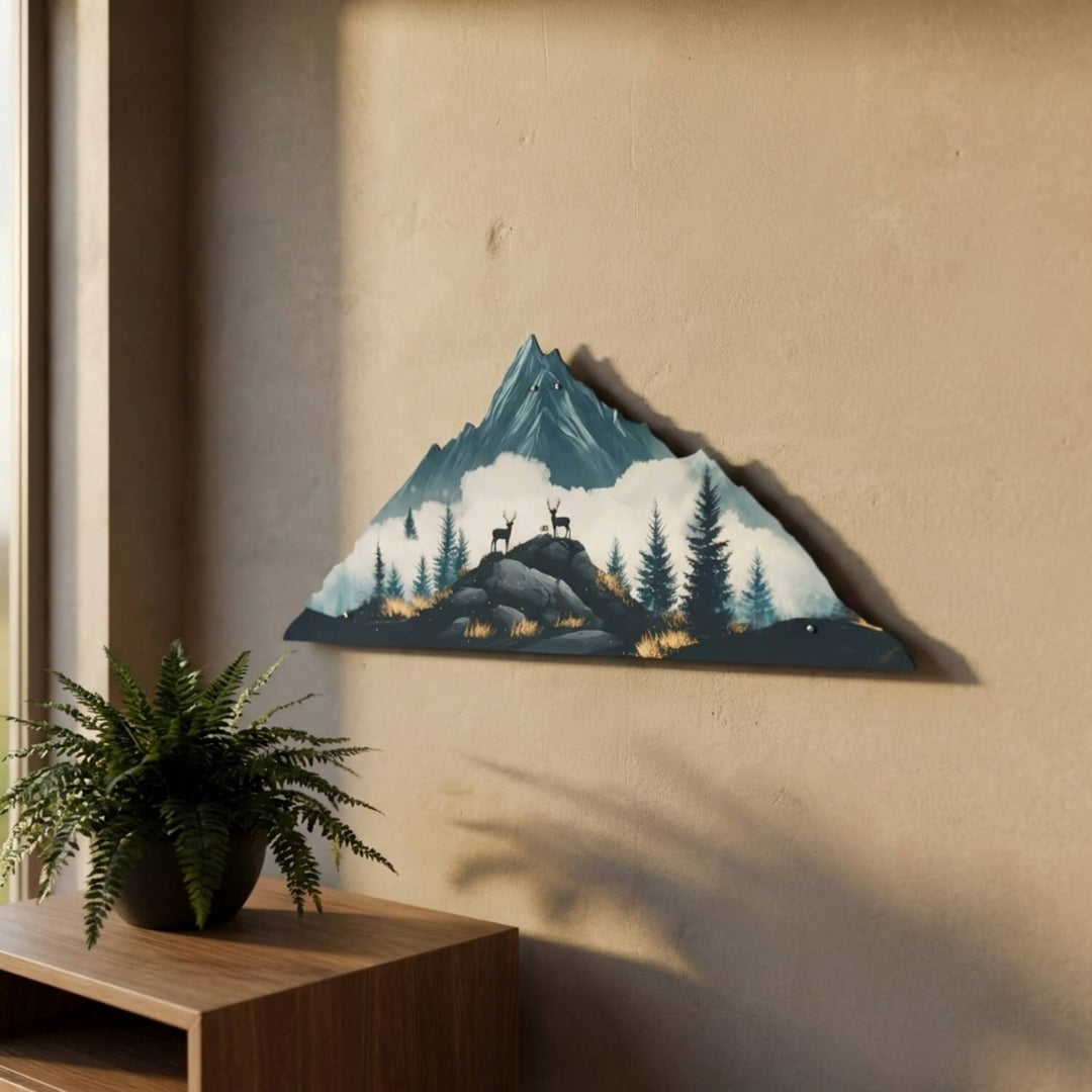 Deer and mountain metal wall art on a beige wall, side view next to a fern