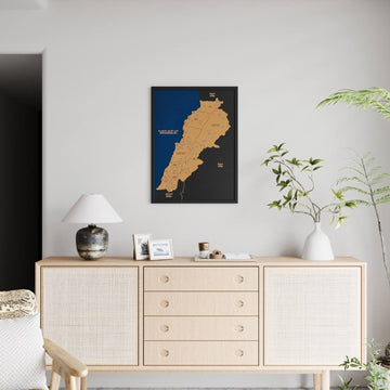 Black-framed Lebanon cork map on a light wall, far view above a full rattan sideboard and lamp