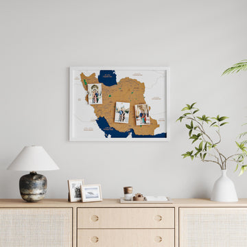 White-framed Iran cork map with three pinned photos, wide view above a rattan sideboard and lamp