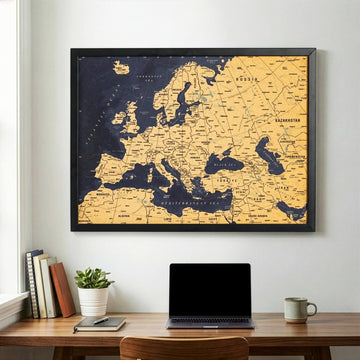 Framed cork map of Europe with a navy sea and cork countries, hung above a wooden desk with a laptop