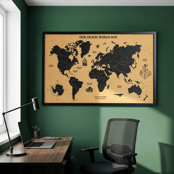 Framed cork world map with black countries and an Our Travel World Map title above a desk against a green wall