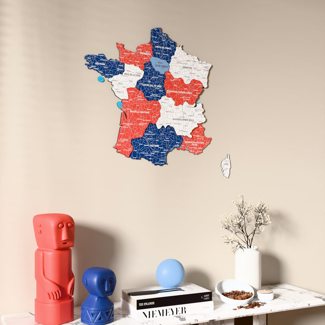 Flag colored France wooden wall map on a beige wall above a console with figurines
