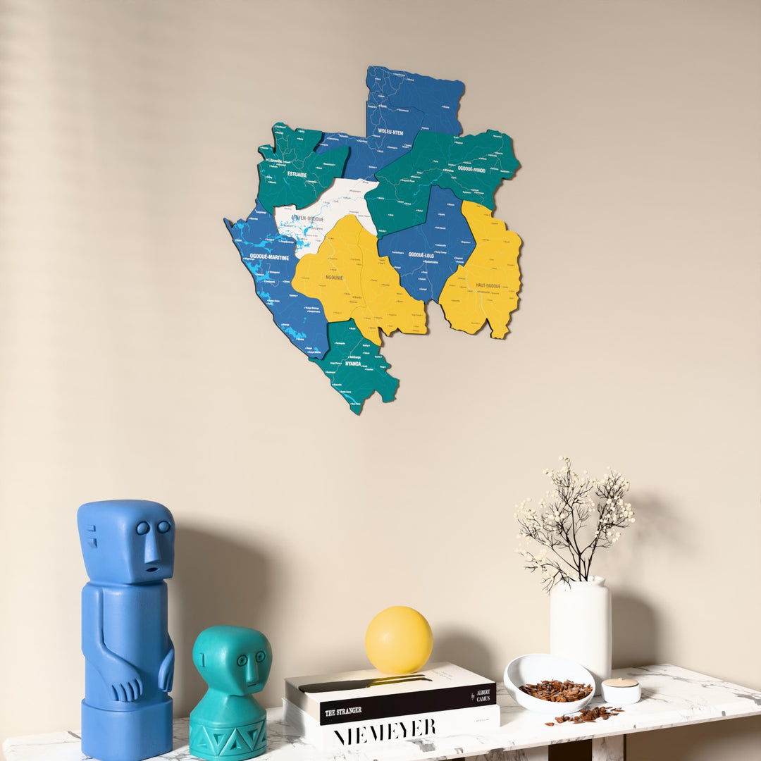 Flag colored Gabon wooden wall map on a beige wall above a console with figurines