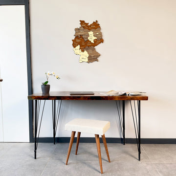 Multicolor wooden Germany wall map hung high above a desk and white stool, wide view of the room