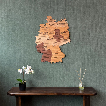 Wooden Germany map on a green textured wall above a dark console with an orchid