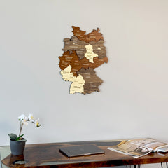 Multicolor 3D wooden Germany map with cities on a gray wall above a desk with an orchid
