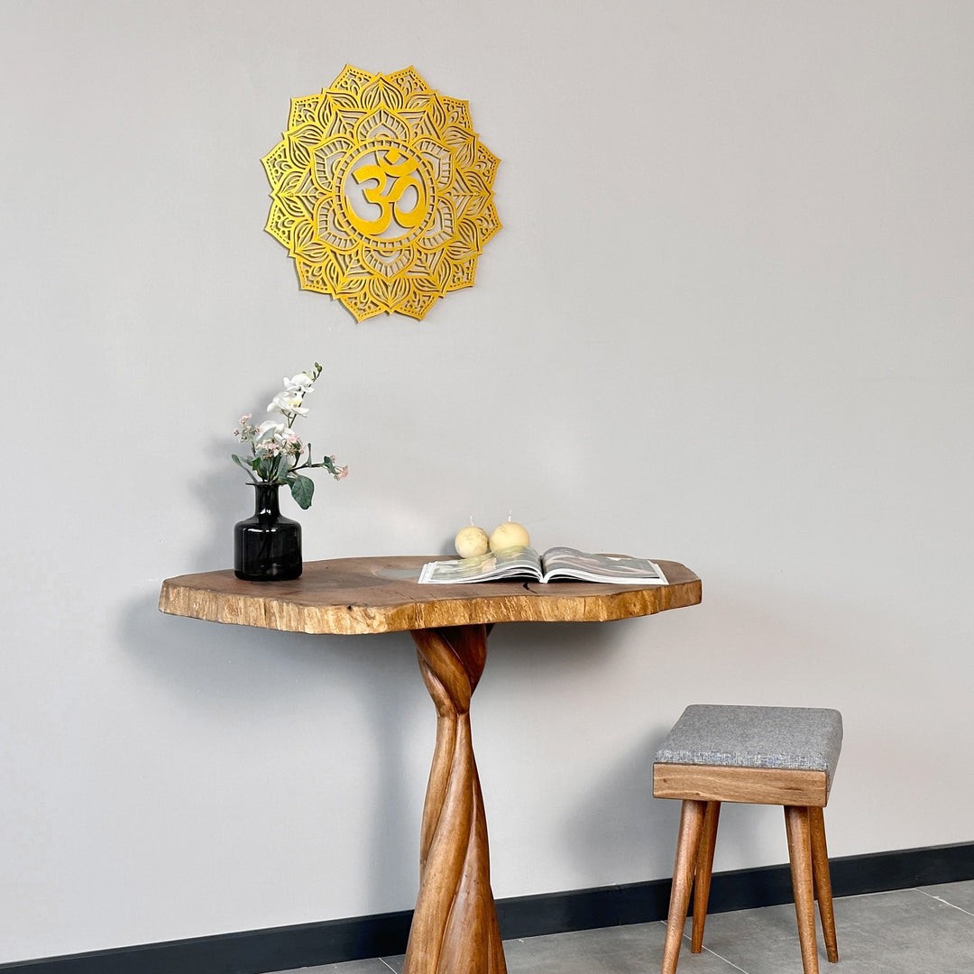 Gold OM mandala metal wall art high on a gray wall above a pedestal table and gray stool, wide view