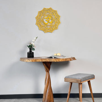 Small gold OM mandala metal wall art above a live-edge pedestal table with a gray stool