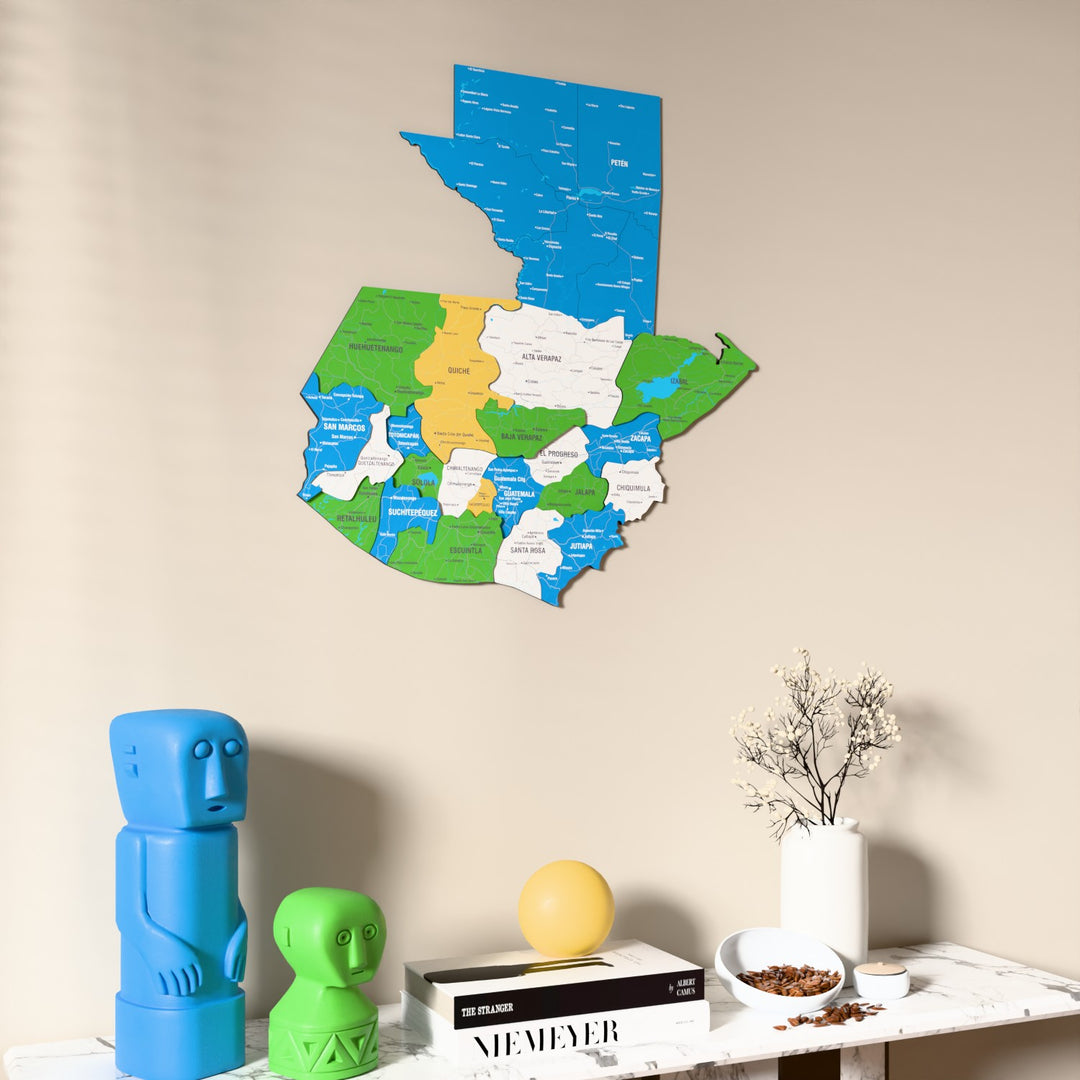 Flag colored Guatemala wooden wall map on a beige wall above a console with figurines
