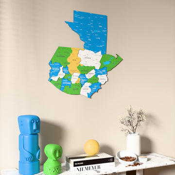 Flag colored Guatemala wooden wall map on a beige wall above a console with figurines
