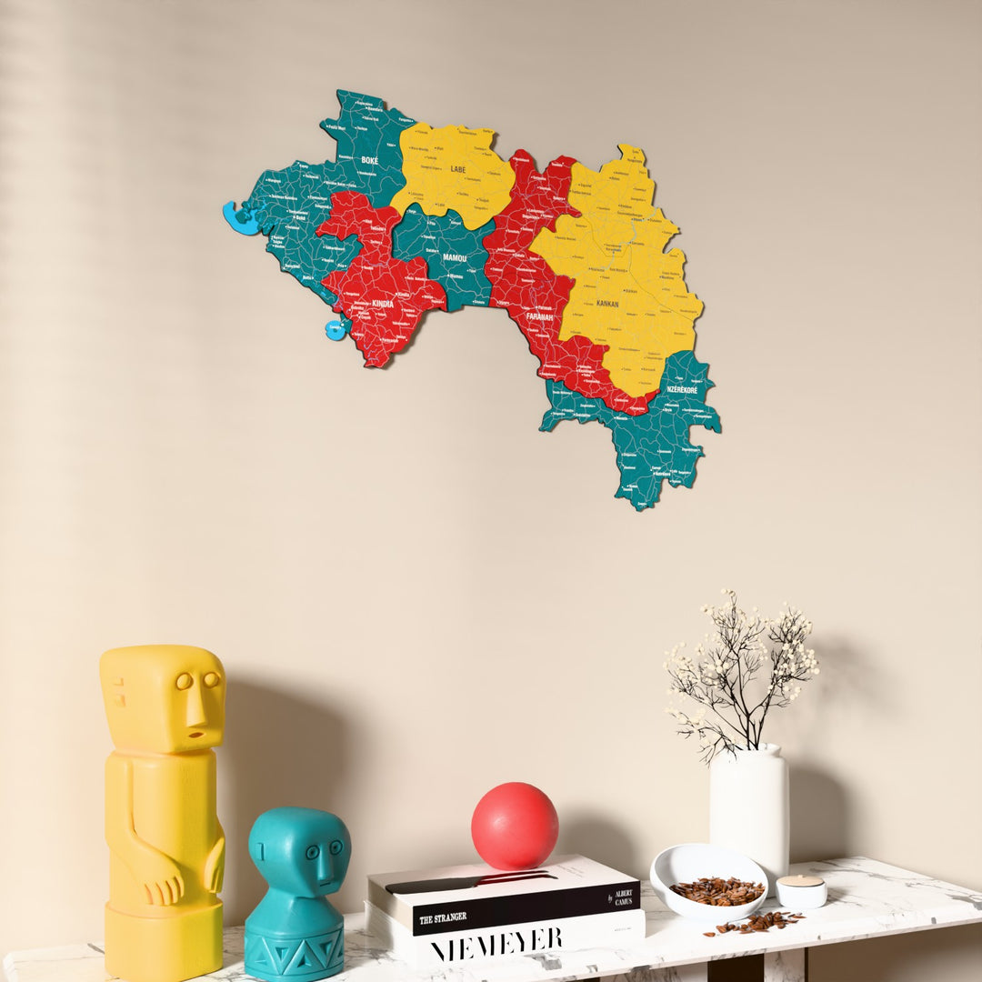 Flag colored Guinea wooden wall map on a beige wall above a console with figurines