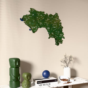 Satellite Guinea wooden wall map on a beige wall above a console with figurines