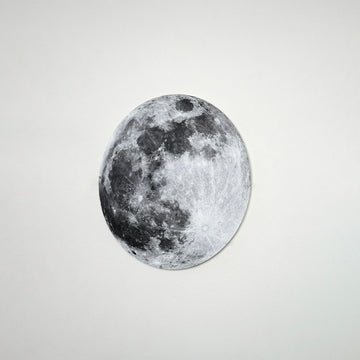 Small metal Moon wall art centered on a white wall, front view with craters and dark maria