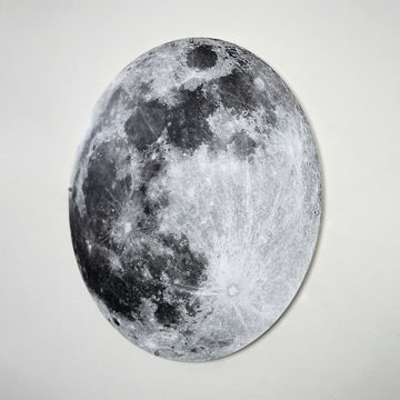 Round metal Moon wall art in light gray tones, angled view showing craters on a white wall