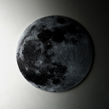 UV printed metal Moon wall art with gray craters, side-lit on a wall fading into shadow
