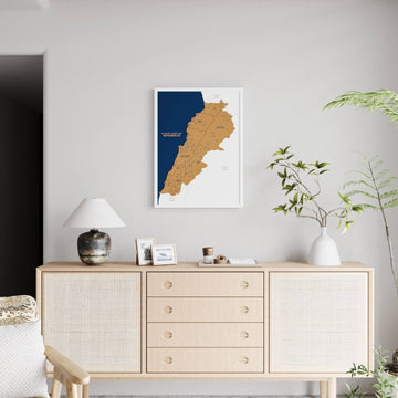 Small white-framed Lebanon cork map on a light wall, far view with a rattan sideboard and lamp