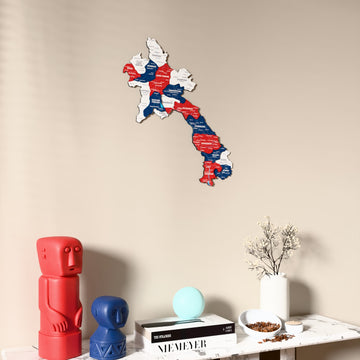 Flag colored Laos wooden wall map on a beige wall above a console with figurines