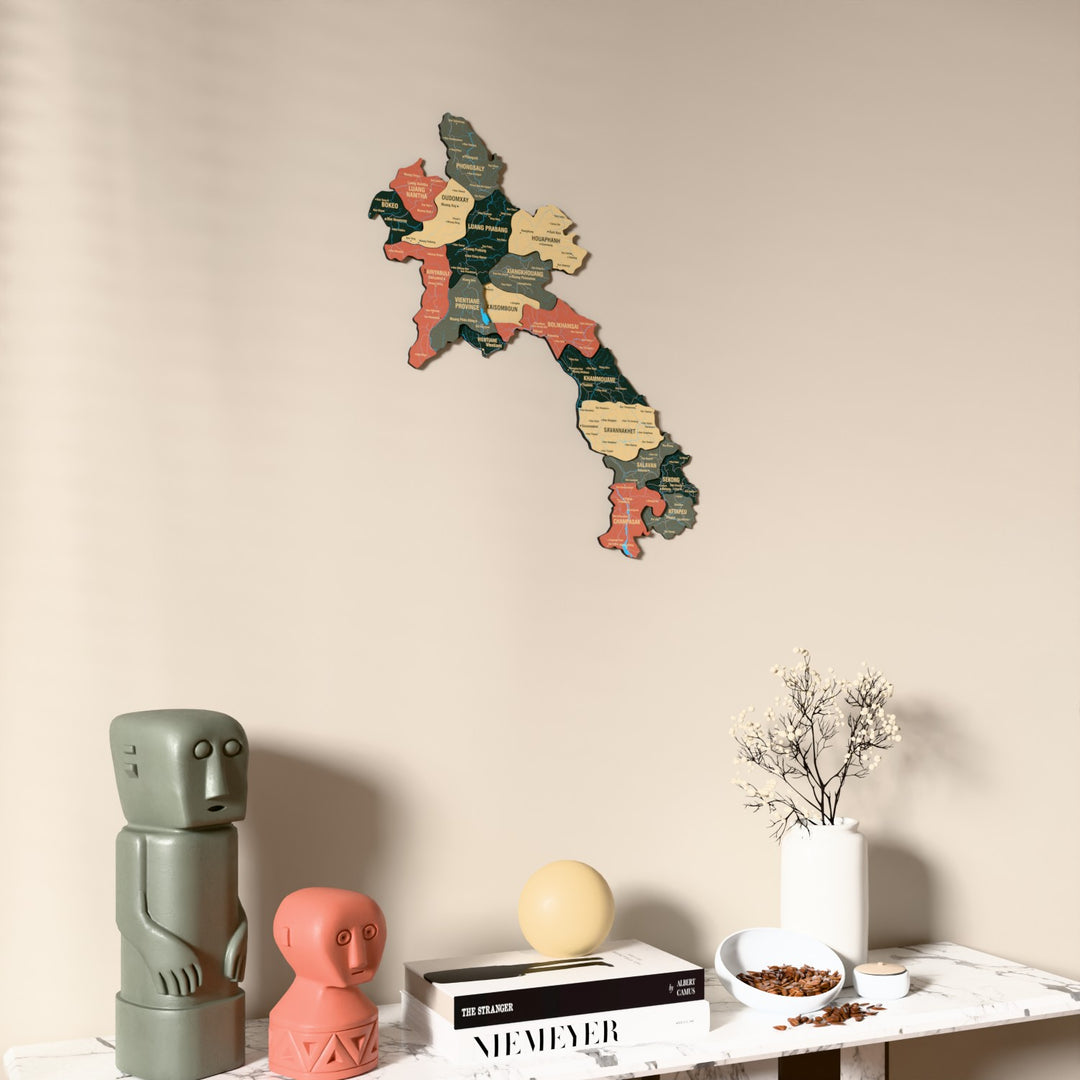 Sage Laos wooden wall map on a beige wall above a console with figurines