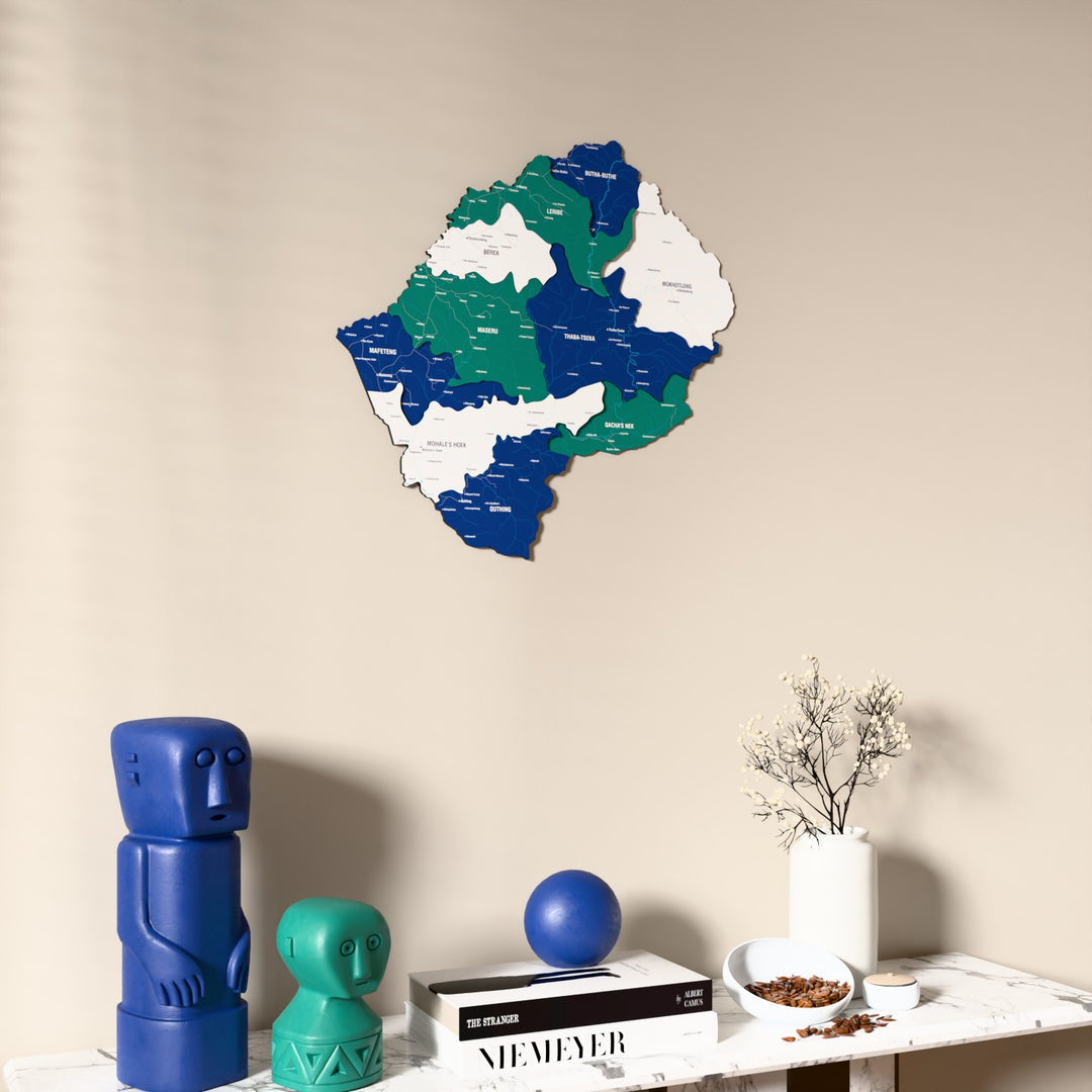 Flag colored Lesotho wooden wall map on a beige wall above a console with figurines