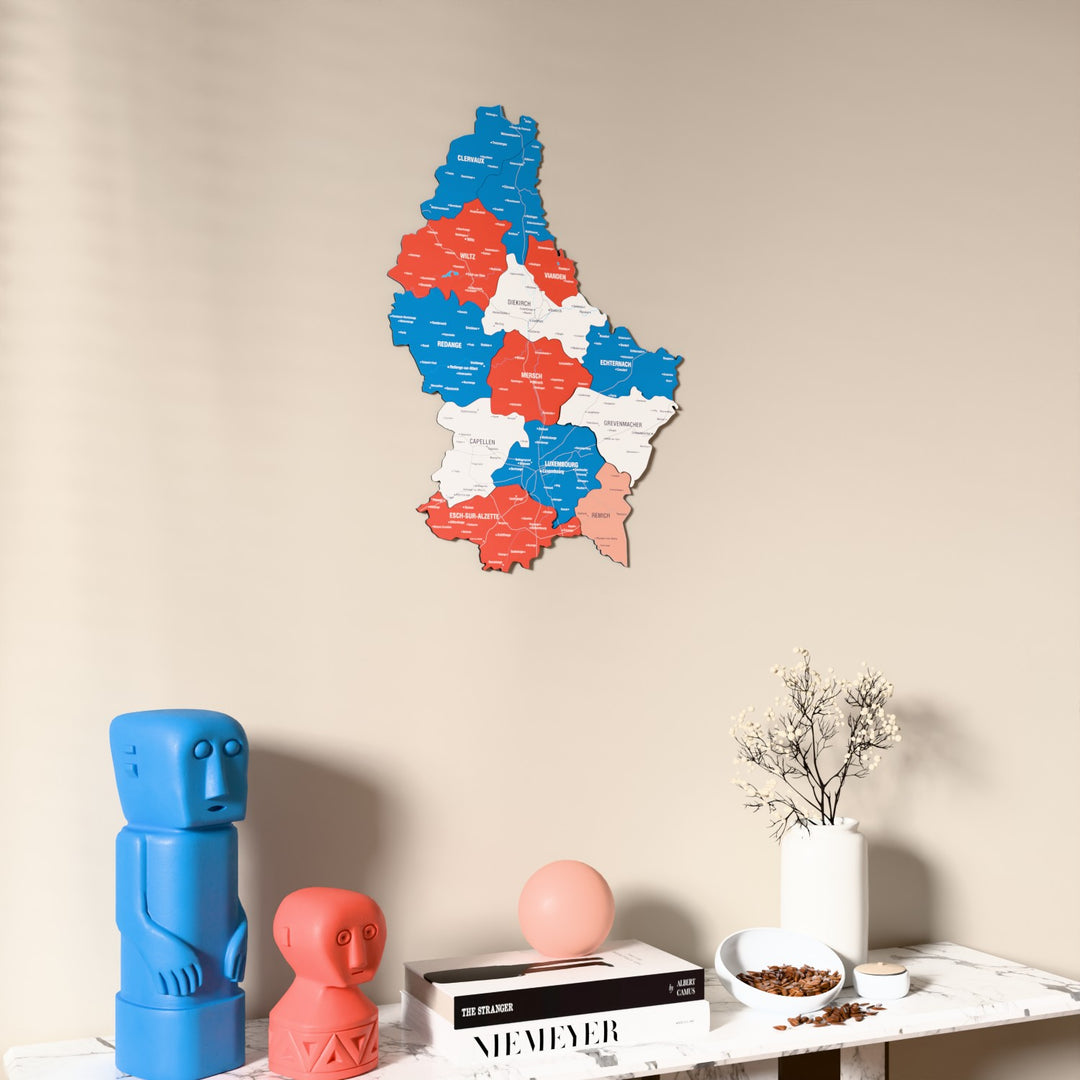 Flag colored Luxembourg wooden wall map on a beige wall above a console with figurines