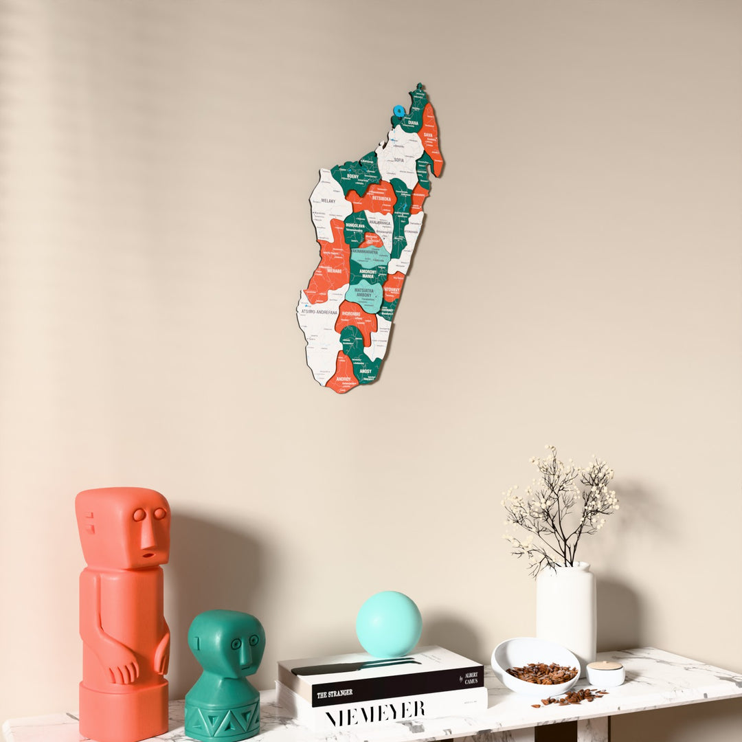 Flag colored Madagascar wooden wall map on a beige wall above a console with figurines
